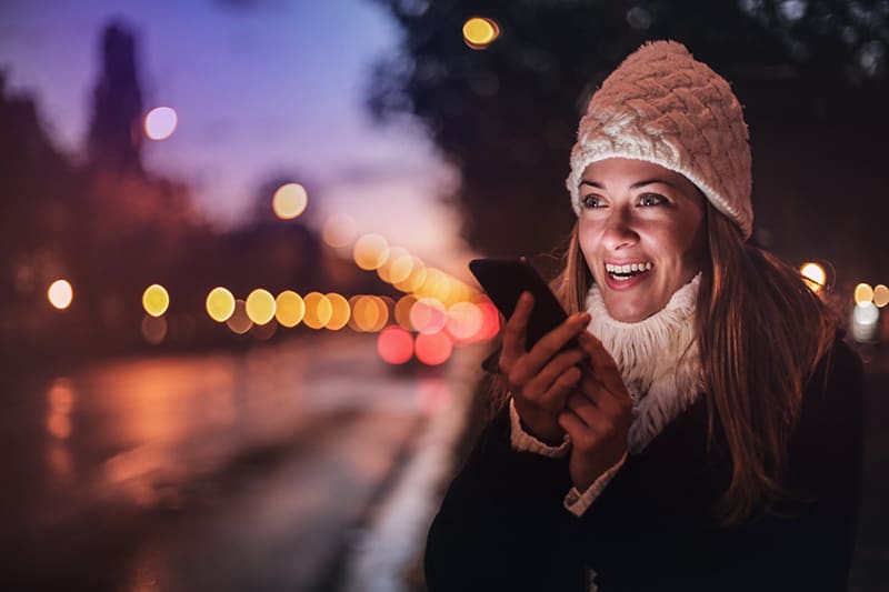 smiling woman holding smartphone while standing in the night