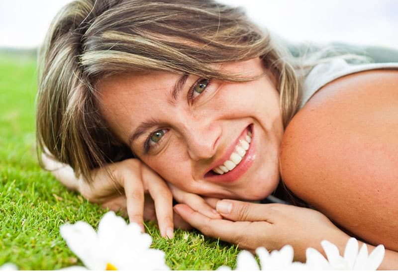 dulce mujer sonriente tumbada en la verde hierba con flores cerca