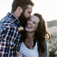 Homem com barba a beijar uma mulher feliz num campo