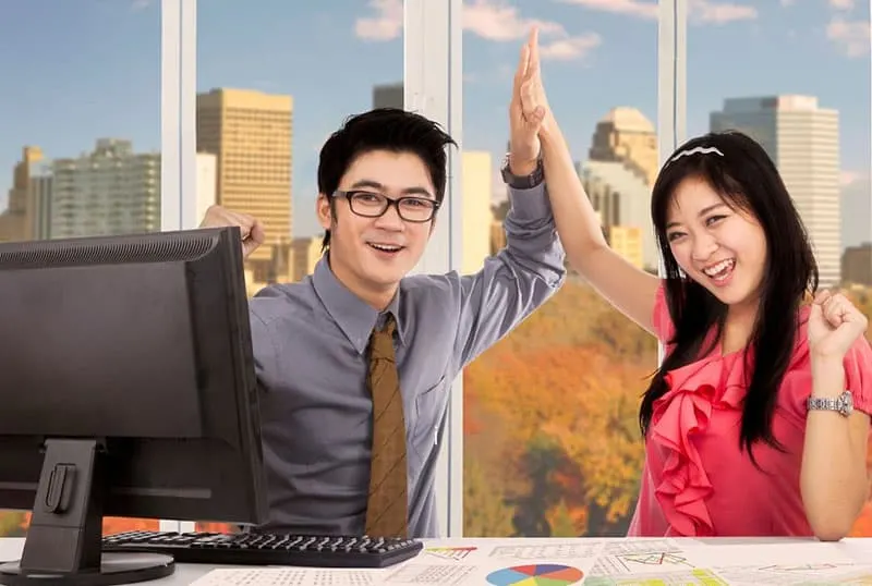 two asian workers celebrating by clapping their hands inside the office