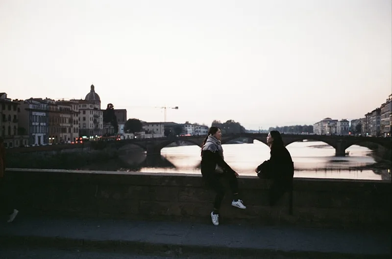 two person sitting on bridge while looking each other