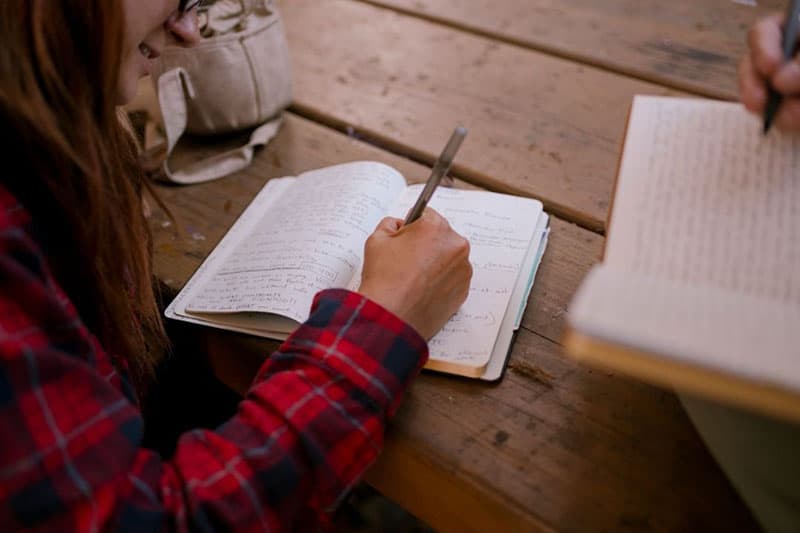 due persone che scrivono su un quaderno su un tavolo di legno