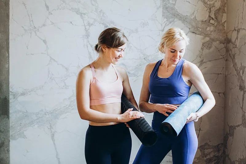 two women standing together while comparing yoga mats