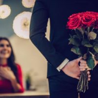 Uomo in piedi di fronte a una donna felice che tiene fiori alle spalle