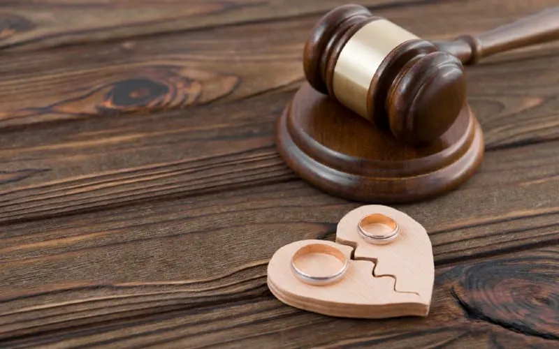 Wedding rings on broken wooden heart near judge hammer on wooden surface