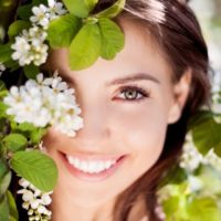 Retrato de mujer feliz en la naturaleza con flores cubriéndole el ojo