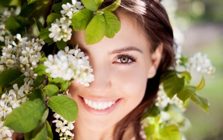 Portrait of happy woman in nature with flowers covering her eye
