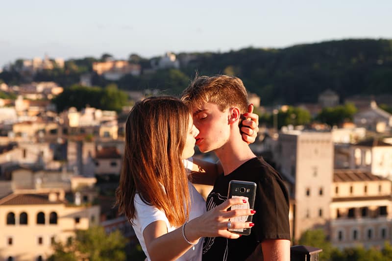 woman about to kiss man while holding smartphone