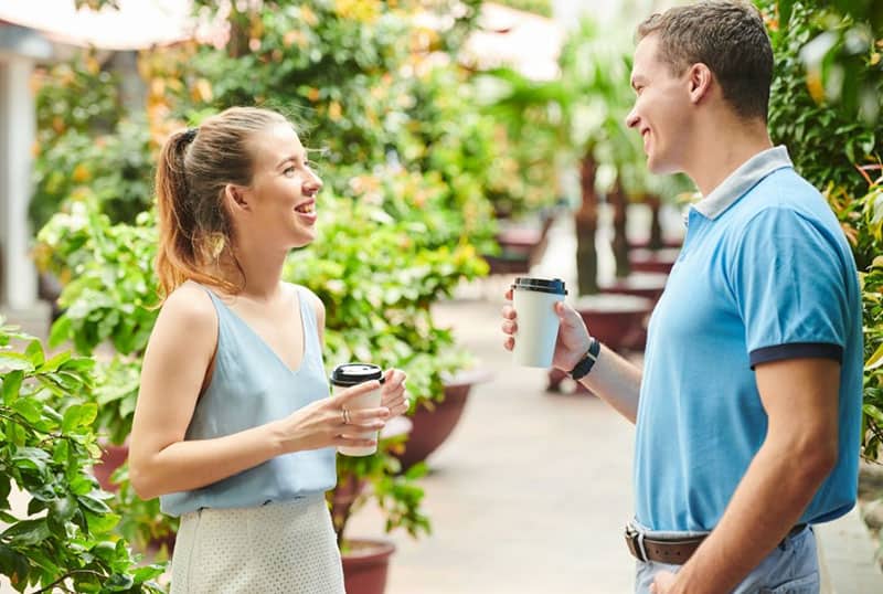 woman and man talking over coffee while standing near walkway and plants