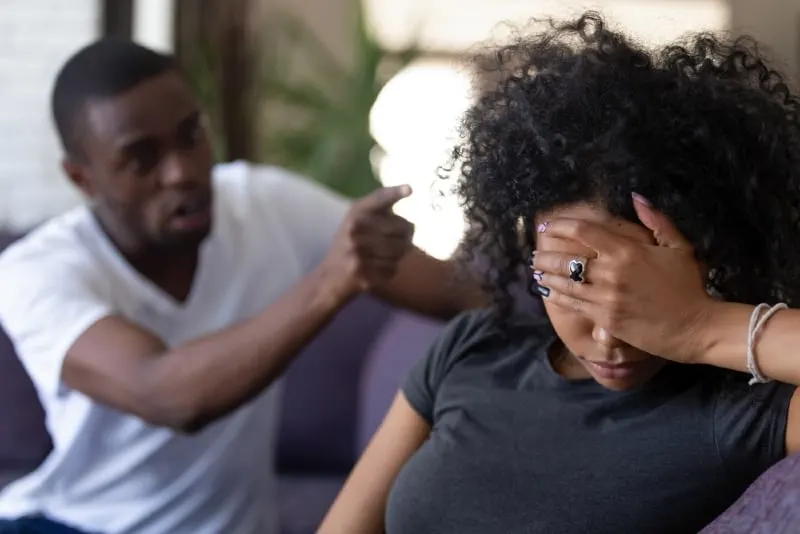 woman covering face with her hand while sitting near angry man