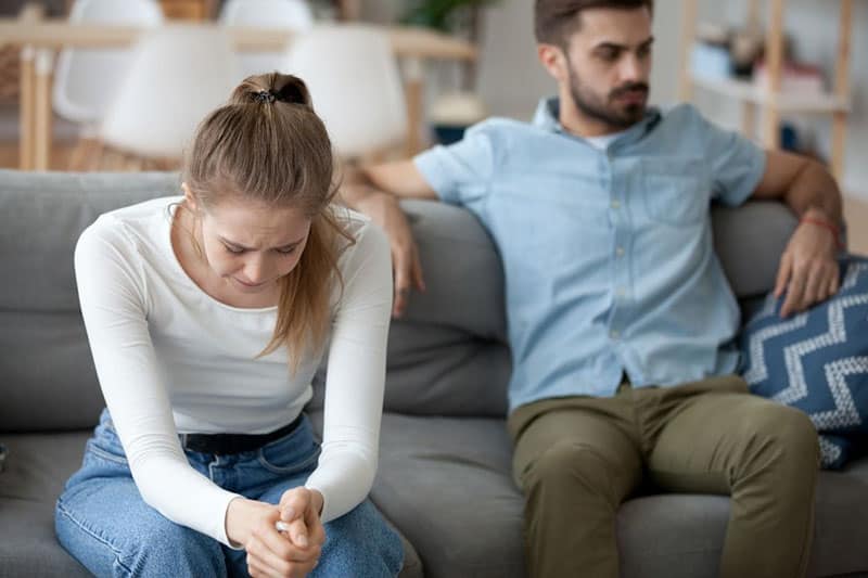 mujer llorando junto a un hombre sentado en un sofá dentro del salón