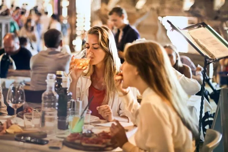 woman drinking wine while sitting at table with another woman