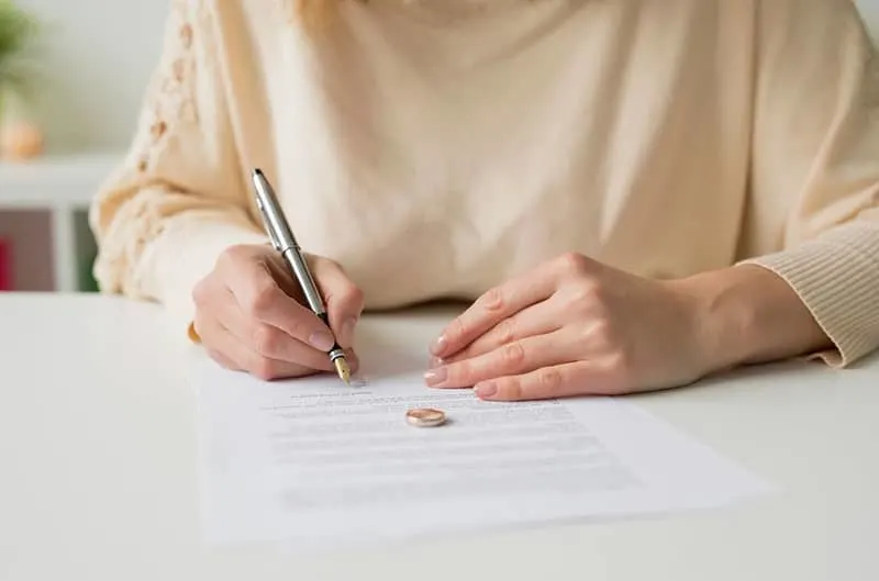 woman going thru divorce signing papers with ring on the paper