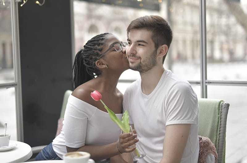 woman holding a flower while kissing a man beside the table