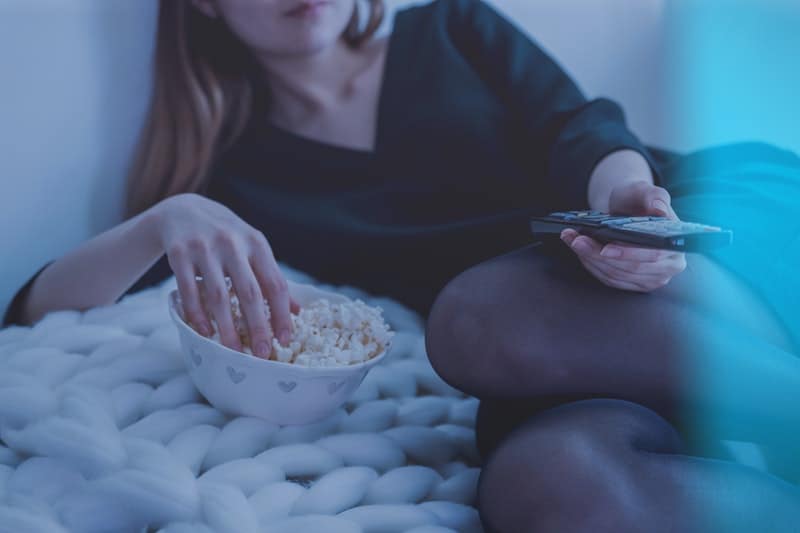 woman holding a remote control and another hand on a bowl of popcorn