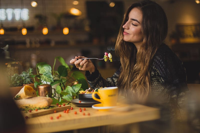 mulher a segurar o garfo enquanto come num restaurante