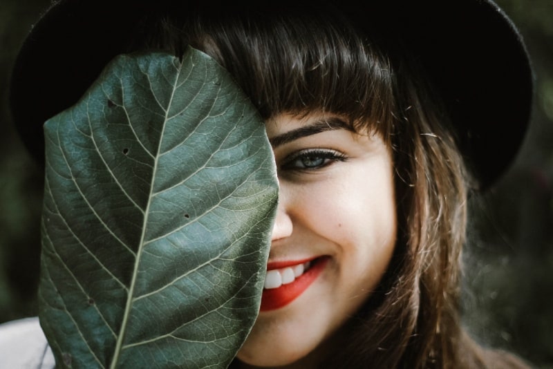 donna sorridente con cappello nero che tiene una foglia