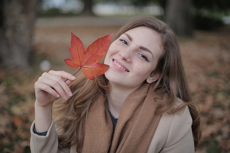 mujer sosteniendo una hoja roja cerca de la cara