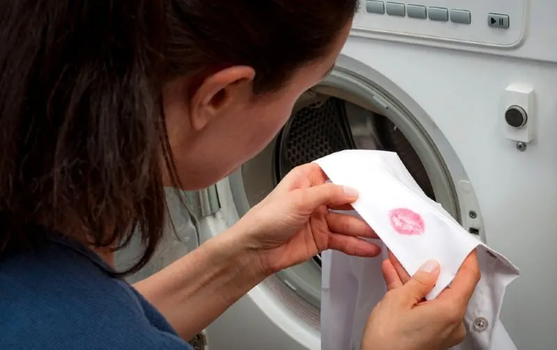 Woman near washing machine holding white man shirt with red kiss lipstick marks
