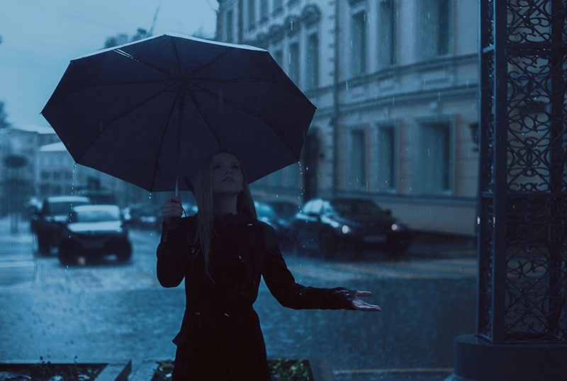 donna che tiene l'ombrello in piedi sulla strada