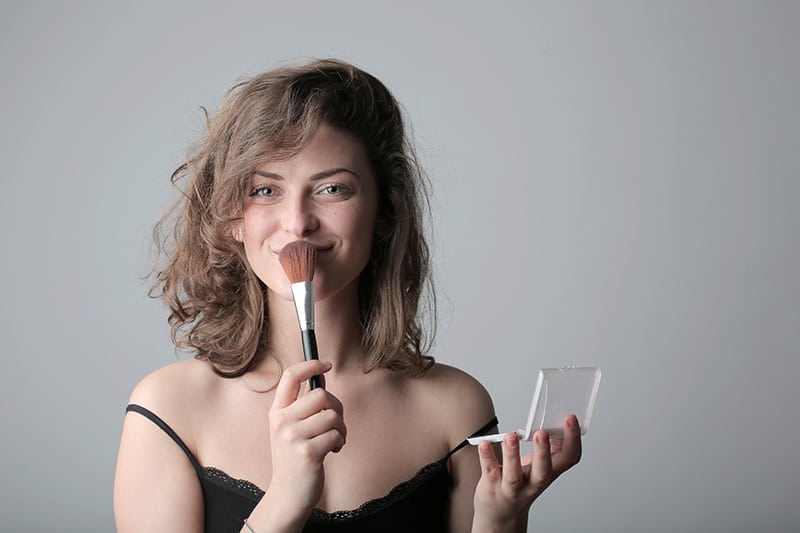 woman in black spaghetti strap top holding makeup brush