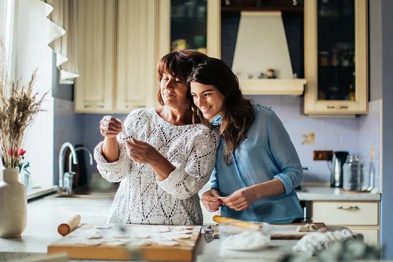 woman in blue long sleeve shirt leaning on her mother while preparing food