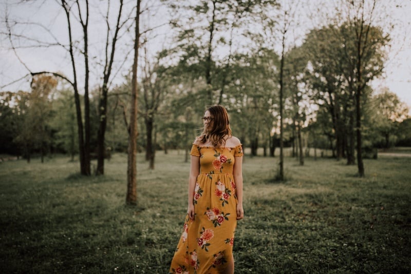 woman in long yellow dress standing in forest