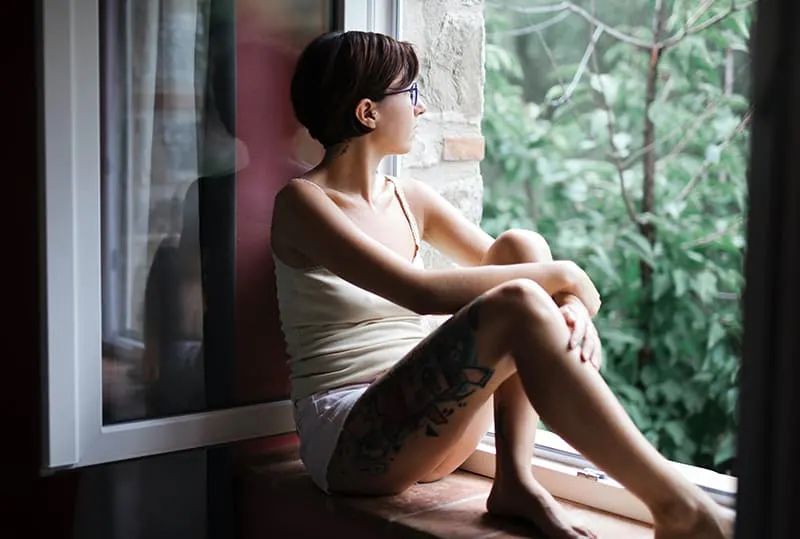 woman in white tank top sitting on window pane