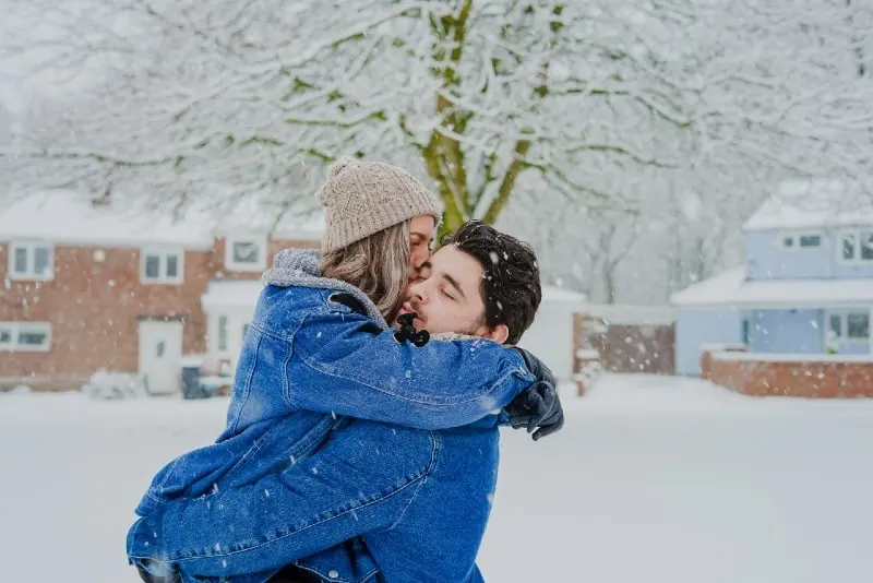 woman with cap kissing man on snow field