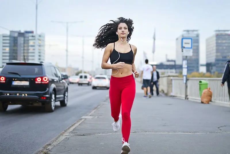 woman listening to music on earphones while running by the sidewalk