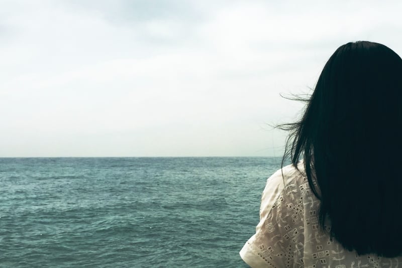 mujer de pelo negro mirando al mar bajo un cielo nublado