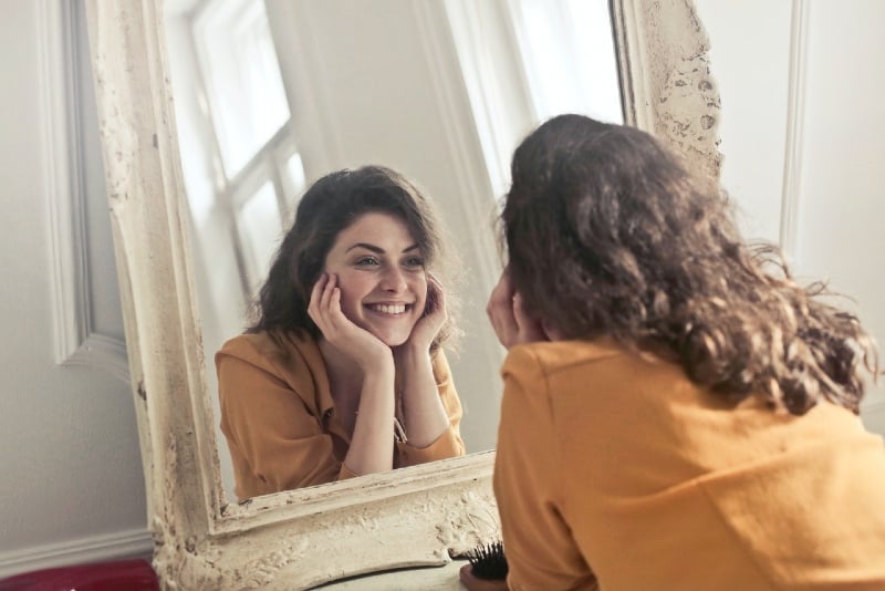 smiling woman in yellow top looking at the mirror