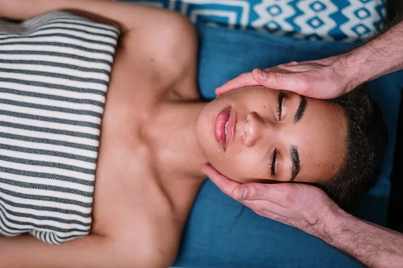 woman lying on blue textile while having face massage