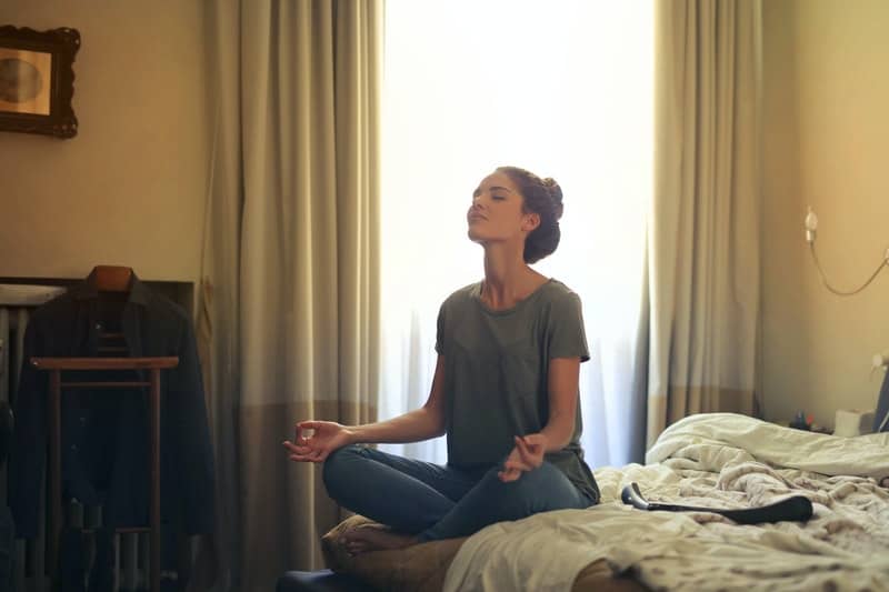 donna che medita in camera da letto facendo posizione yoga sul letto