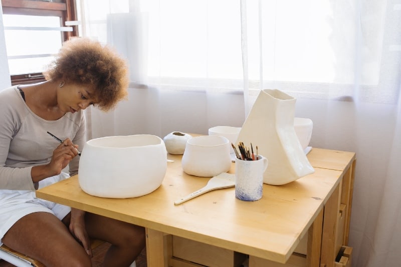 woman painting ceramic bowl while sitting on chair