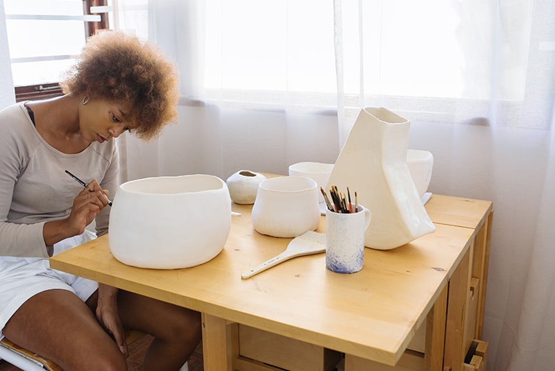 woman painting ceramic bowl while sitting beside table