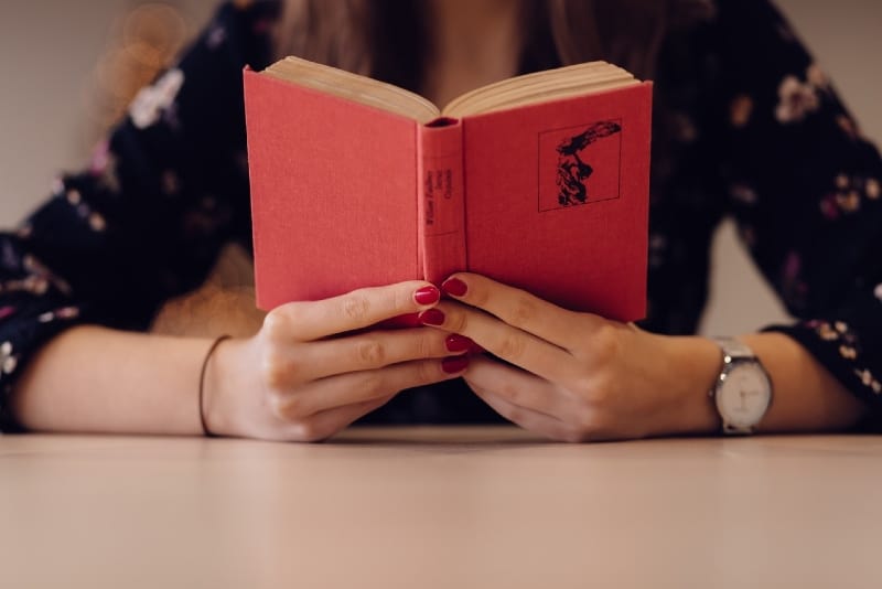 mujer con uñas rojas y reloj leyendo un libro