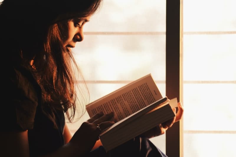donna che legge un libro seduta vicino alla finestra