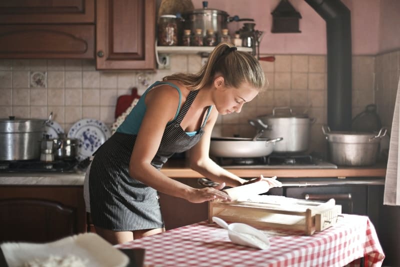 mujer enrollando masa para hornear en la cocina