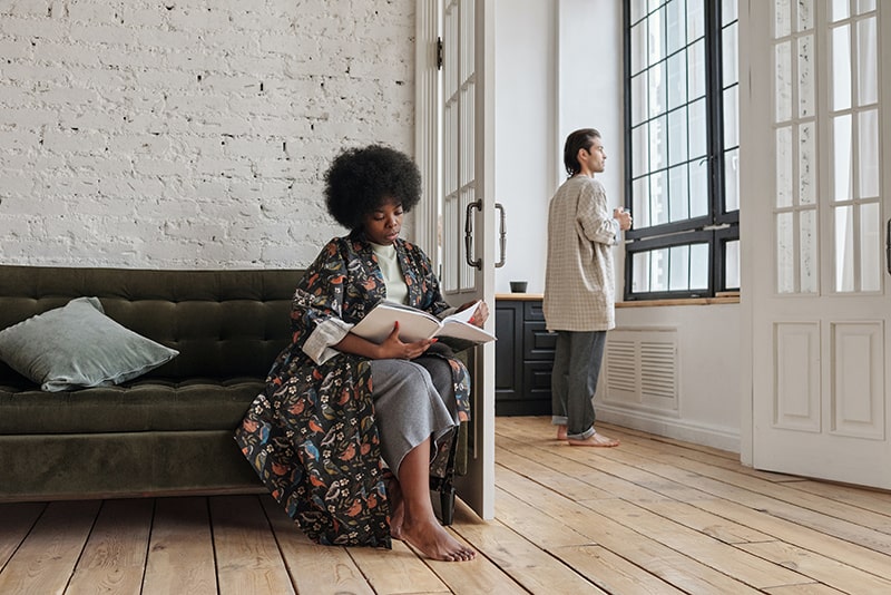 woman sitting on a couch and reading a magazine while men standing beside the window