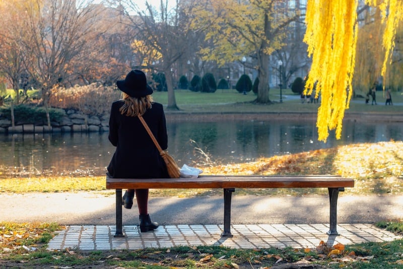 woman with black hat sitting on bench looking at water