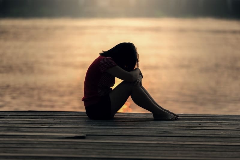 mujer triste sentada en un muelle de madera cerca del agua