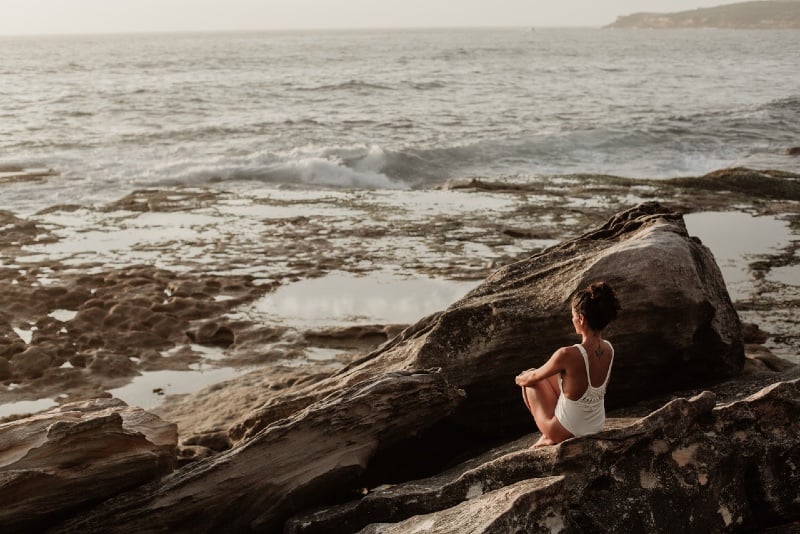 woman in white swimsuit sitting on rock