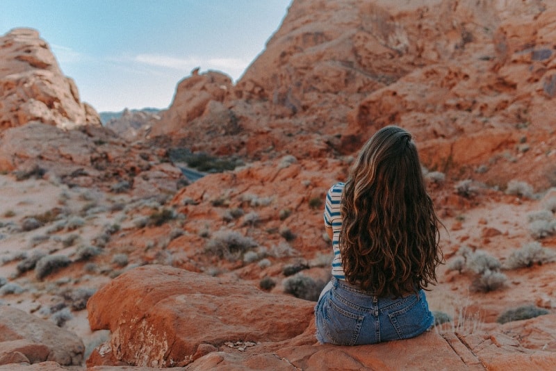 donna in pantaloncini di jeans seduta su una roccia marrone