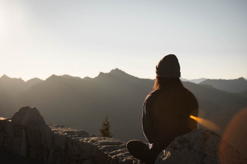 mujer con gorra sentada en una piedra mirando la montaña