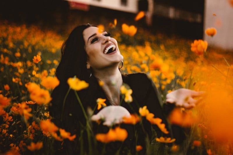 mujer sonriente sentada en el campo cerca de flores amarillas