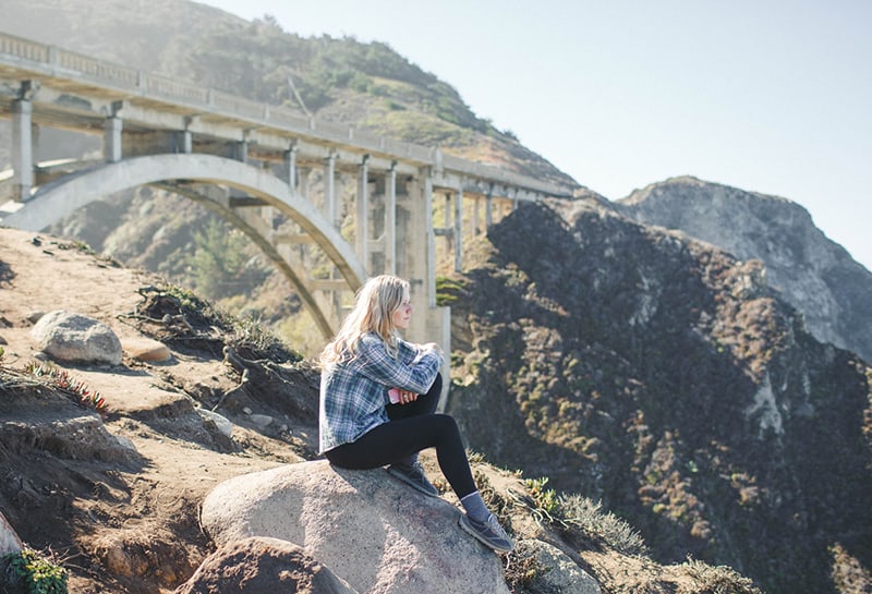 woman sitting on the rock under the bridge