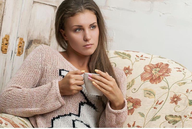 donna seduta con una tazza in mano che pensa indossando un maglione