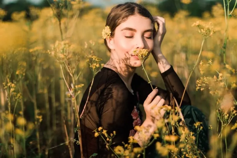 woman in black top smelling yellow flower