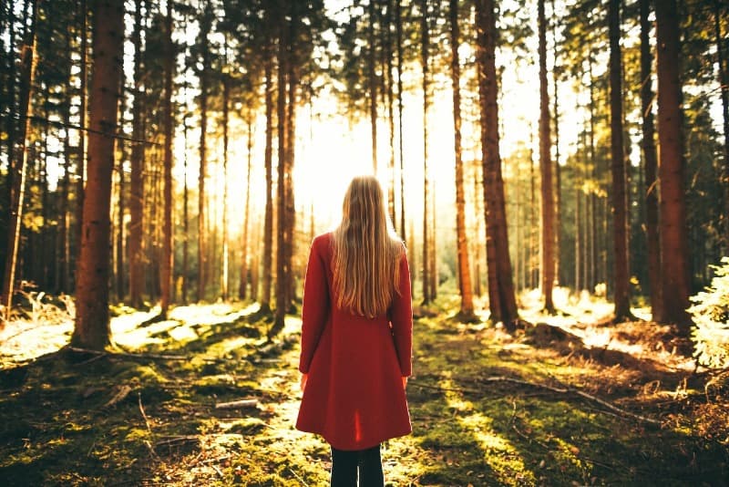 blonde woman in red coat standing in forest